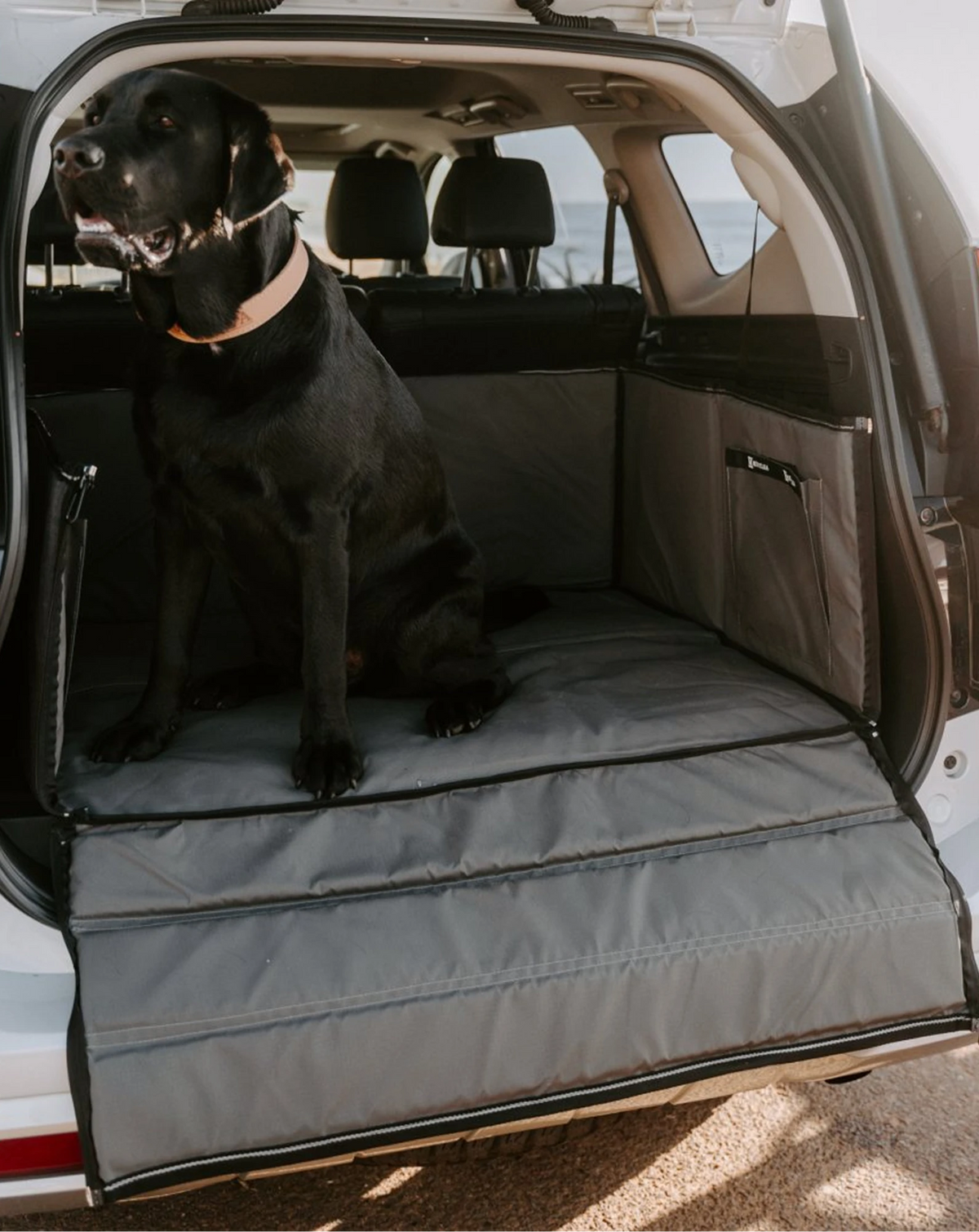 Black Labrador sitting on a Huntlea boot bed in the back of an SUV